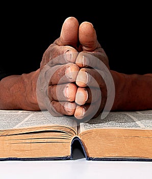 Praying to god with hands together on the bible Caribbean man praying with black background stock photo