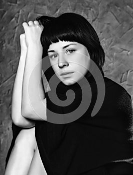 Praying woman in black dress with hood on a grey background. black and white