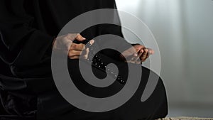 Praying woman with traditional islamic beads in hand kneeling on rug in mosque
