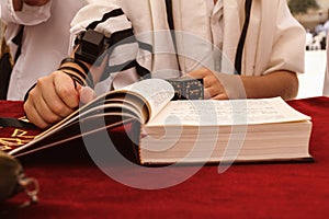 A praying young man hands with a tefillin holding a bible book, while reading a pray at a Jewish ritual