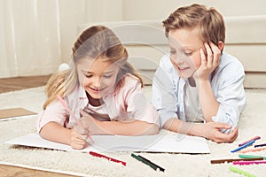 Pre-adolescent kids drawing pictures while lying on the floor at home