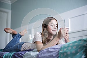 Pre-adolescent teen girl texting on a smartphone lying in bed at home