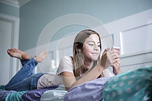Pre-adolescent teen girl texting on a smartphone lying in bed at home photo