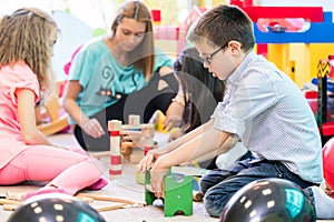 Pre-school boy cooperating with kids under guidance of kindergar