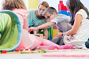 Pre-school boy cooperating with kids under guidance of kindergar