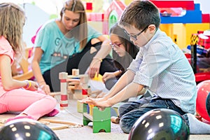 Pre-school boy cooperating with kids under guidance of kindergarten teacher