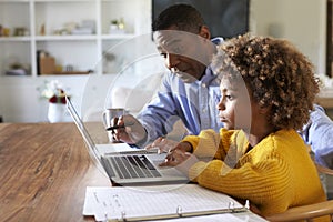 Pre teen girl African American  girl using a laptop computer sitting at table in the dining room with her home tutor, selective fo