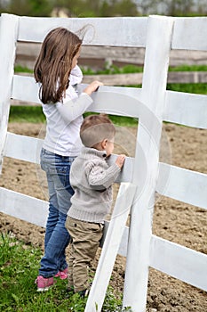 Pre-teen girl and Baby boy on the a white picket fence beside th