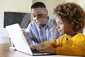 Pre teen girl African American  girl using a laptop computer sitting at table in the dining room with her home tutor, close up, se