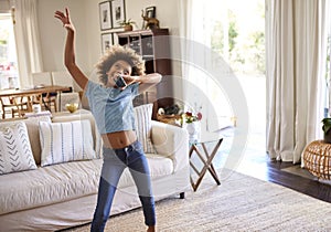 Pre-teen girl dancing and singing along to music in the living room at home using her phone as a microphone, three quarter length