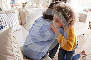 Pre-teen girl hugging her mother sitting on sofa in the living room, elevated, back view