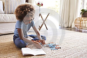 Pre-teen girl sitting on the floor in the living room reading instructions and constructing a model, close up photo