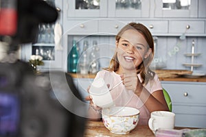 Pre-teen girl video blogging in kitchen mixing ingredients