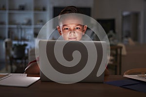 Pre-teen Hispanic boy sitting at dining table doing his homework using a laptop computer, close up