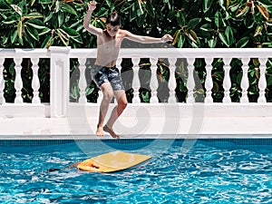 Pre-teens play in the pool by jumping on a small surfboard to keep their balance