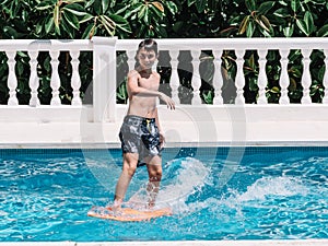 Pre-teens play in the pool by jumping on a small surfboard to keep their balance