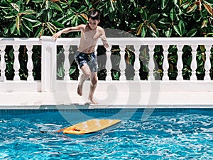 Pre-teens play in the pool by jumping on a small surfboard to keep their balance