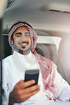 Pre work planning in commute. Shot of a young muslim businessman using his phone while traveling in a car.