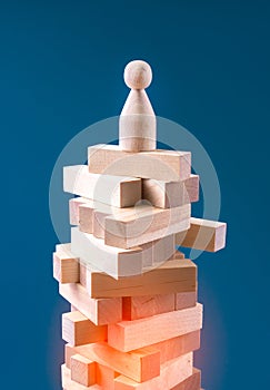 Precarious business situation concept with wooden human figurine standing on wooden blocks.
