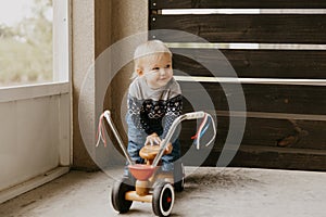 Precious Adorable Cute Little Blonde Baby Toddler Boy Kid Playing Outside on Wooden Toy Bicycle Scooter Mobile Smiling at the Came