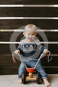 Precious Adorable Cute Little Blonde Baby Toddler Boy Kid Playing Outside on Wooden Toy Bicycle Scooter Mobile Smiling at the Came