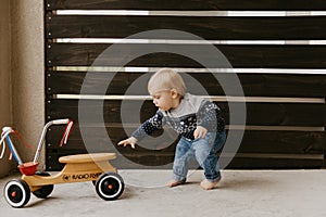 Precious Adorable Cute Little Blonde Baby Toddler Boy Kid Playing Outside on Wooden Toy Bicycle Scooter Mobile Smiling at the Came