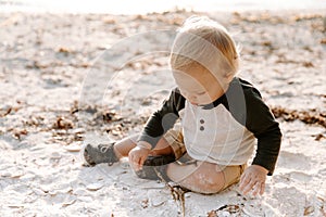 Precious Adorably Cute Happy Baby Boy Toddler Smiling and Playing in the Sand At the Beach Next to the Ocean Water Outside During