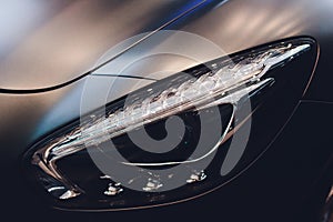 Predatory car headlight and hood of powerful sports grey car with blue glare.