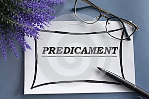 PREDICAMENT - word on a white sheet against the background of glasses, pens and lavender