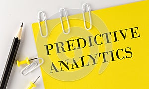 PREDICTIVE ANALYTICS word on the yellow paper with office tools on the white background