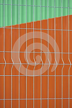 Prefabricated grating wire fence panel with blurred background of orange steel wall and green metal roof
