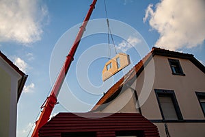 Prefabricated house part with windows between two houses is transported by the mobile crane for assembly