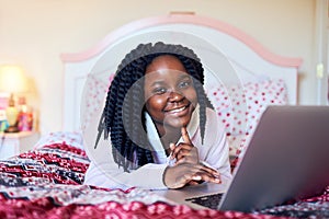 She prefers doing her homework on her device. Shot of an adorable little girl using a laptop while lying on her bed in