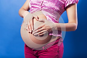 Pregnan woman in casual outfit cherish her belly. blue background