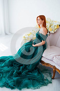 Pregnancy beauty. Beautiful elegant readhead pregnant woman in green dress posing in tender home interior.