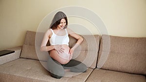 Pregnancy concept. Beautiful married pregnant woman rubbing belly and talking with child. Happy future mother sitting on sofa at h