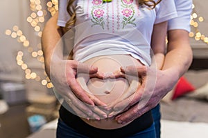 Pregnancy concept - couple making a heart shape with their hands on the pregnant belly. Hands of family members holding a belly of