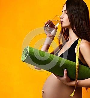 Pregnancy concept. Pregnant woman drinking water hold sport green yoga mat for workout and tape measure