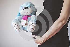 Pregnancy concept. Pregnant woman holding teddy bear toy in his hand, studio isolated