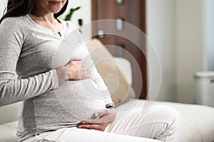 Pregnancy concept, pregnant woman touching belly with hands sitting on couch