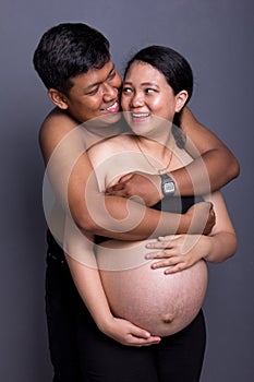 Pregnancy couple embracing and smiling to each other, on grey