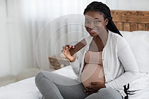 Pregnancy Cravings. Smiling Expectant Black Woman Eating Milk Chocolate Bar At Home photo