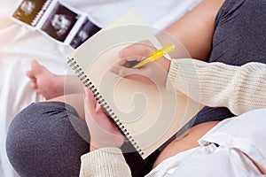 Pregnancy dairy Pregnant woman writing schedule in notebook for memory Mother sit on bed