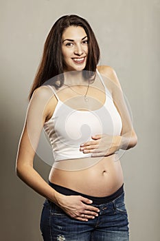 Pregnancy and expectation concept - happy pregnant woman and touching her belly, gray background, portrait