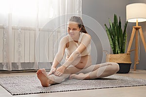 Pregnancy fitness at home. Care for pregnant body. Adorable brown haired pregnant woman exercising while sitting on floor