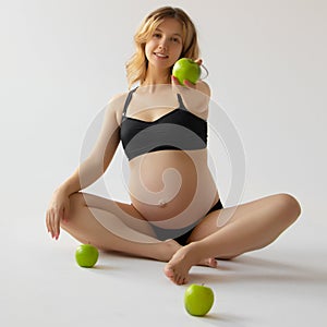 Pregnancy, healthy food and people concept close up of happy pregnant woman eating green apple at studio