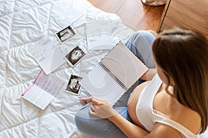 Pregnancy list woman writing. Beautiful pregnant woman writing check list. Happy pregnancy lady holding notepad. Concept