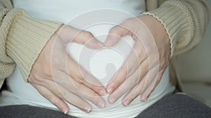 pregnancy  love  people and expectation concept - happy pregnant woman making heart gesture over holidays lights background.