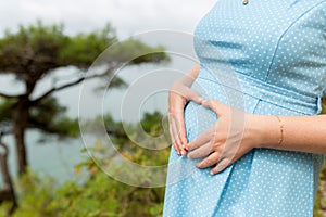 Pregnancy, love, people and expectation concept - happy pregnant woman making heart gesture over sea background