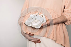 Pregnancy, maternity, preparation, baby expectation concept. Pregnant woman in pink dress holding small shoes for unborn